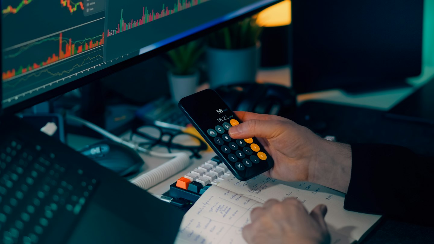 Dłonie używające kalkulatora w smartfonie nad notatnikiem finansowym.